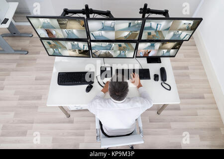 Security System Operator Looking At CCTV Footage At Desk Stock Photo