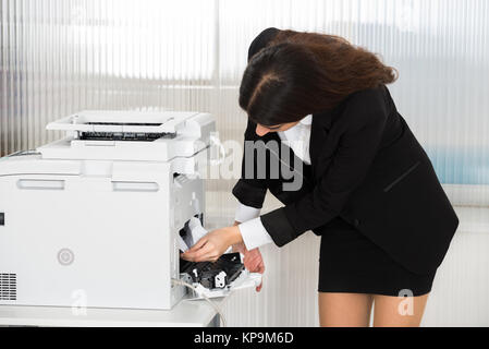 Businesswoman Removing Paper Stuck In Printer At Office Stock Photo