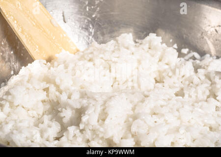 Cooked white rice in a metal bowl and wooden spoon stirrer Stock Photo