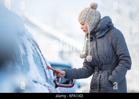 Young woman cleaning her car from snow and frost on a winter morning Stock Photo
