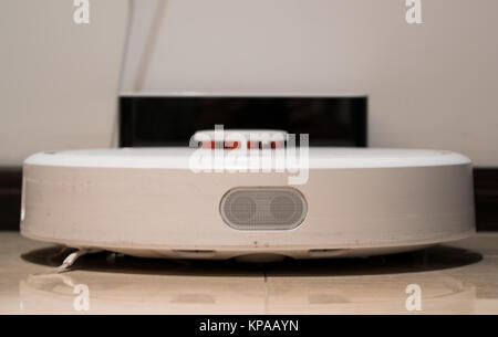 Generic white robotic vacuum cleaner front view recharging on the base Stock Photo