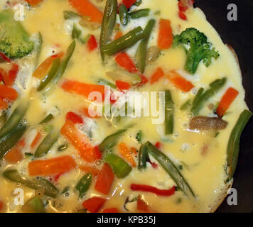 Nutritious one egg and two egg whites Omelet cooking in a non stick skillet.  Frozen veggies of beans, broccoli carrots and diced red peppers added Stock Photo