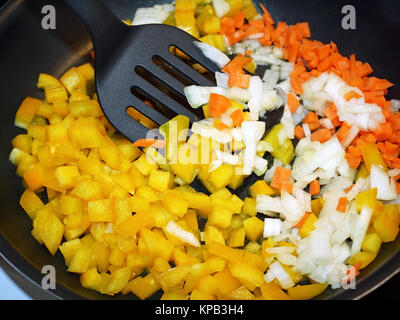 Diced raw carrots, white onions and yellow peppers in non stick skillet ready for cooking Stock Photo