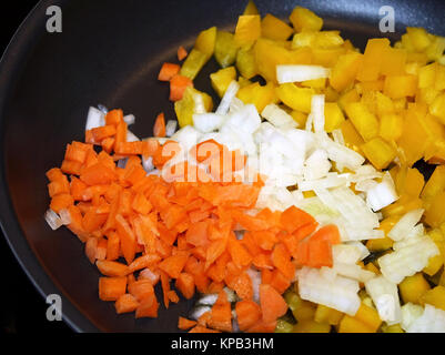 Diced raw carrots, white onions and yellow peppers in non stick skillet ready for cooking Stock Photo