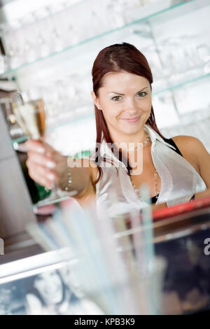 Model release, Junge Bardame mit Sektglas hinter der Theke - young barmaid with sparkling wine behind bar Stock Photo