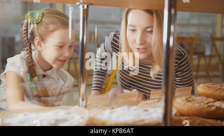 Girl with a pigtail and her mom look at the pies in the window choosing Stock Photo