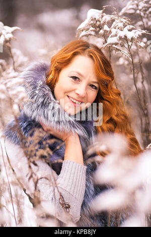 Portrait of beautiful young woman over winter snowy wood background. Closeup of female smiling face with gorgeous long ginger hair. Stock Photo