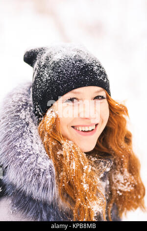 Portrait of beautiful young girl dressed in fur coat and black hat at winter snowy trees background. Beauty woman having fun outside in wood on winter Stock Photo