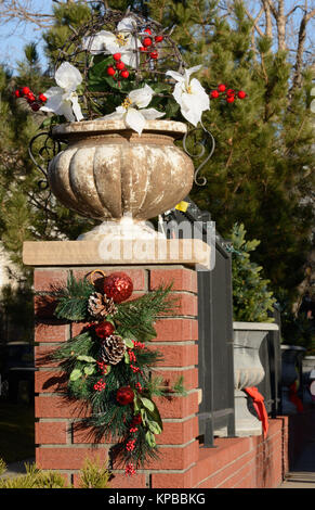 Christmas decorations propped on brick wall entrance with poinsettia leaves, berries, pine cones, pine branches and Christmas ball ornaments Stock Photo