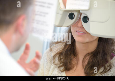 female patient looking through phoropter during eye exam Stock Photo