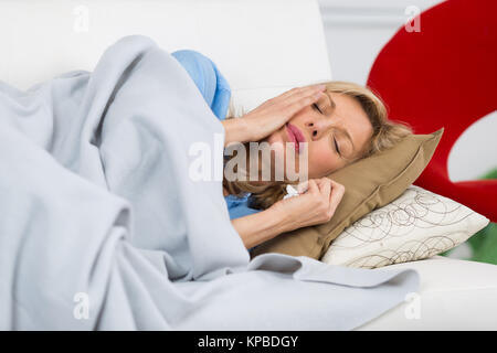 sick mature woman laying on the couch at home Stock Photo