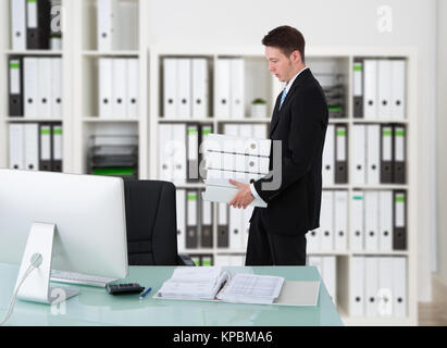 Businessman Carrying Binders By Desk Stock Photo