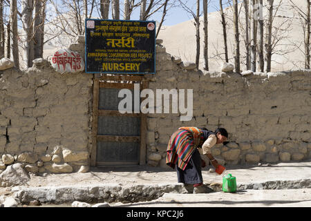 Tibetan woman filling a watering can from the communal  water supply in Lo Manthang, Upper Mustang region, Nepal. Stock Photo