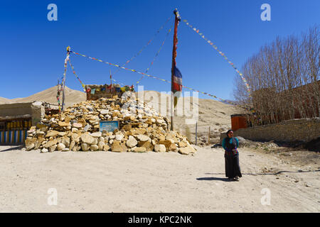 Tibetan woman walking past a pile of praying stones in Lo Manthang, Upper Mustang region, Nepal. Stock Photo
