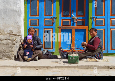 Young Tibetan mother holding her son beside an older woman who is spinning Himalayan sheep wool, Lo Manthang, Upper Mustang region, Nepal. Stock Photo