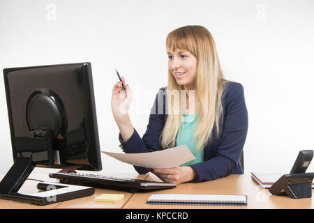 Happy business woman working at a computer and holding a piece of paper and a pen Stock Photo