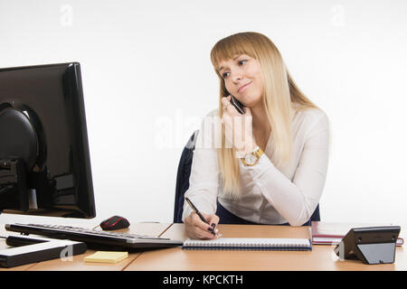 Upset secretary writing in a notebook the information obtained over the phone and looked at the screen Stock Photo
