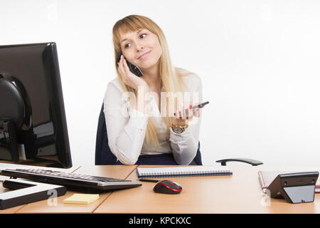 Happy secretary looked at the computer screen talking on the phone working and holding a cell Stock Photo