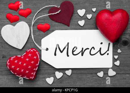 Label With Red Textile Hearts On Wooden Gray Background. French Text Merci Means Thank You. Retro Or Vintage Style. Black And White Image With Colored Hot Spot. Stock Photo
