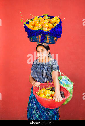 ANTIGUA, GUATEMALA - DEC 23, 2015; Unknown young Guatemalan woman carries fruit in a baskets at her head and hands on Dec 23, 2015, Antigua, Guatemala Stock Photo