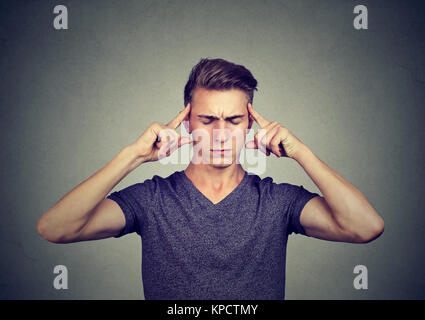 Young casual man touching temples trying to focus on something important keeping eyes closed. Stock Photo