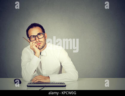 Young office worker sitting at table distracted from work process and daydreaming. Stock Photo