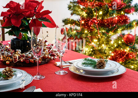 Christmas or New Years table decoration concept - champagne glasses, red poinsettia and table setting on a background of colorful Christmas decoration Stock Photo
