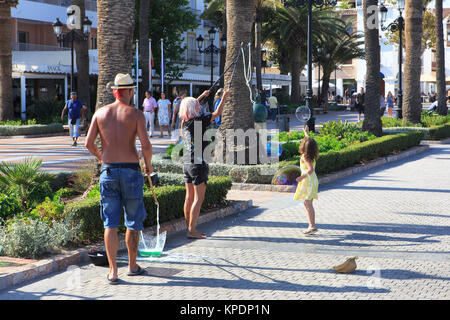 A small girl trying to catch a huge soap bubble made by an artistic performer at the Balcon de Europa in Nerja on the Costa del Sol in Spain Stock Photo