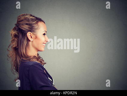 Side view of young woman posing on gray backdrop smiling cheerfully. Stock Photo