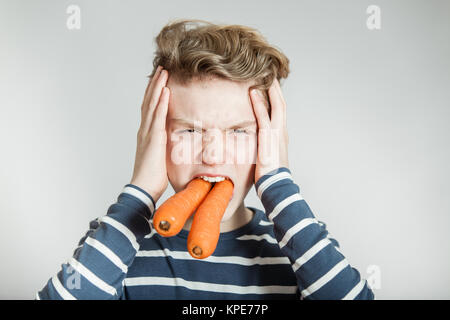 Boy Holding Head with Two Large Carrots in Mouth Stock Photo