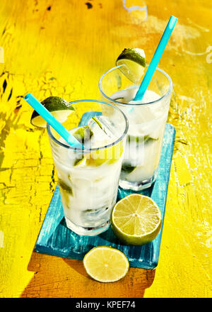 High Angle View of Pair of Brazilian Caipirinha Cocktails Made from Fresh Lime, Sugar and Cachaca Served in Tall Glasses with Blue Straws on Rustic Yellow Painted Wooden Table Stock Photo