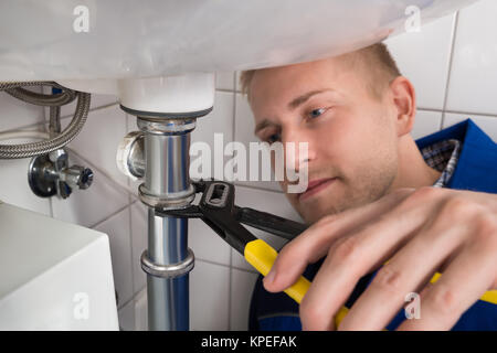 Young Male Plumber Fixing Sink In Kitchen Stock Photo