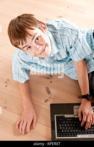 Cute teenaged boy using computer on floor Stock Photo
