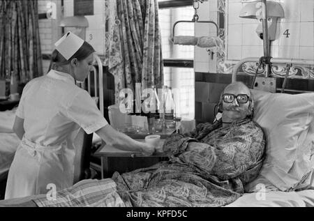 1970S NHS  Charing Cross Hospital London nurse giving patient a cup of tea. Listening and watching Tv with head phones so silent in ward 1972  England HOMER SYKES Stock Photo