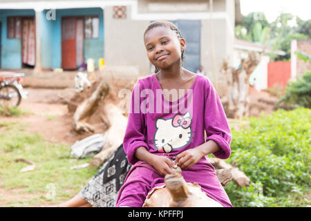 A beautiful laughing Ugandan girl sitting on a fallen tree trunk. Stock Photo