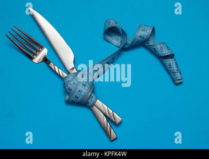 Knife and fork wrapped in tape measure on blue Stock Photo
