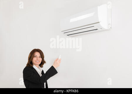 Businesswoman Operating Air Conditioner Stock Photo