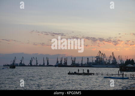 Cranes in the port on the shore of the Sea under the rays of the evening sun Stock Photo
