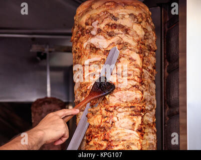 Gyros or doner, Middle East traditional food. Man's hands holding a knife, cutting slices from a vertical skewer Stock Photo