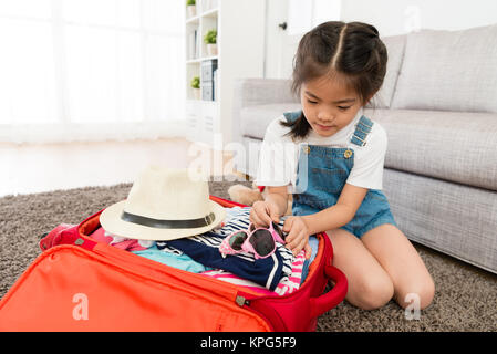 beautiful young little girl put sunglasses in travel luggage suitcase when she preparing go to trip with family during summer vacation. Stock Photo