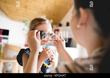 Mother puts on sunglasses to her cute little daughter. Stock Photo
