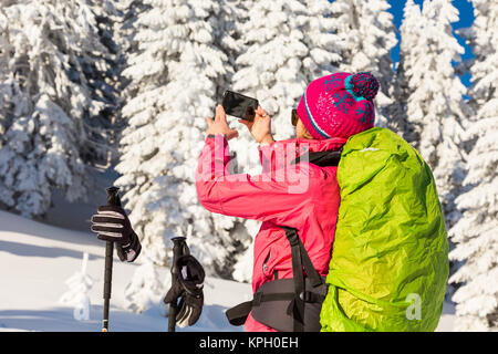 Caucasian woman in colorful outfit taking a break from backcountry skiing taking a picture, recording the beautiful winter scenery Stock Photo