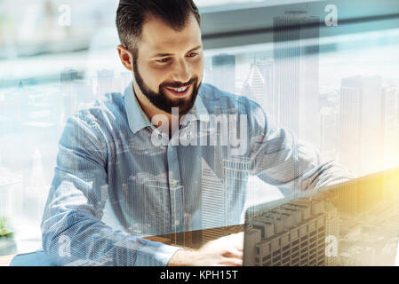 Handsome joyful man smiling and using his computer. Stock Photo