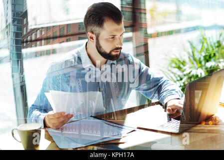 Adult occupied man keeping papers and using the laptop. Stock Photo