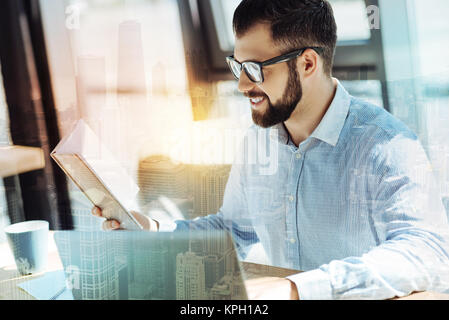 Pleasant joyful man smiling and reading the book. Stock Photo