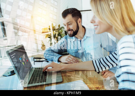 Two pleasant satisfied workers smiling and using the laptop. Stock Photo