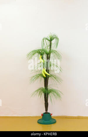 Artificial green palm with yellow bananas is on stand Stock Photo