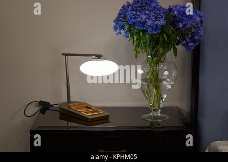 Lamp, nightstand and a bunch of blue hydrangea flowers in bedroom Stock Photo