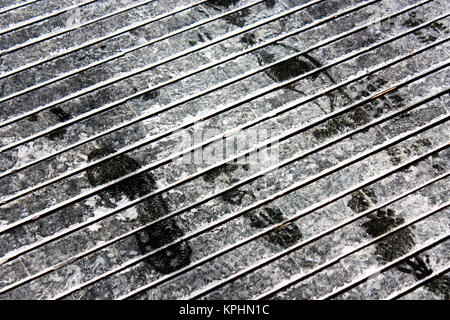 Wet shoe prints on dry anti slip pattern sidewalk with road salt white marks  in winter in black and white Stock Photo