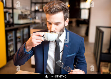 Handsome businessman stricly dressed in the suit drinking coffee at the modern cafe interior Stock Photo